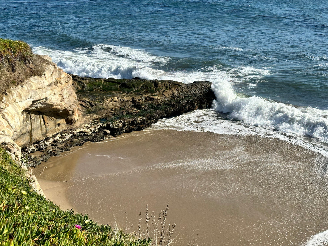 Looking downward at the ocean and a small beach surrounded by cliffs.