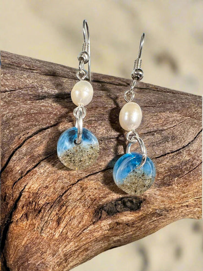 This is a photo of earrings, circle of sand and resin, freshwater pearl accent, and french hooks.