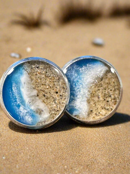 This is picture of earrings with sand and resin representing an ocean coast. 