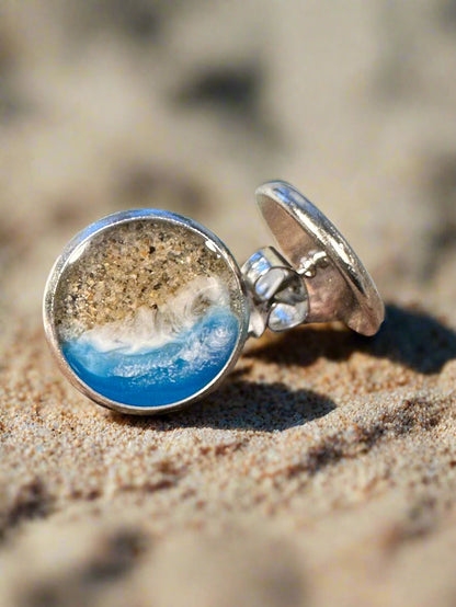 This is a picture of round earrings with sand and resin representing the coast.