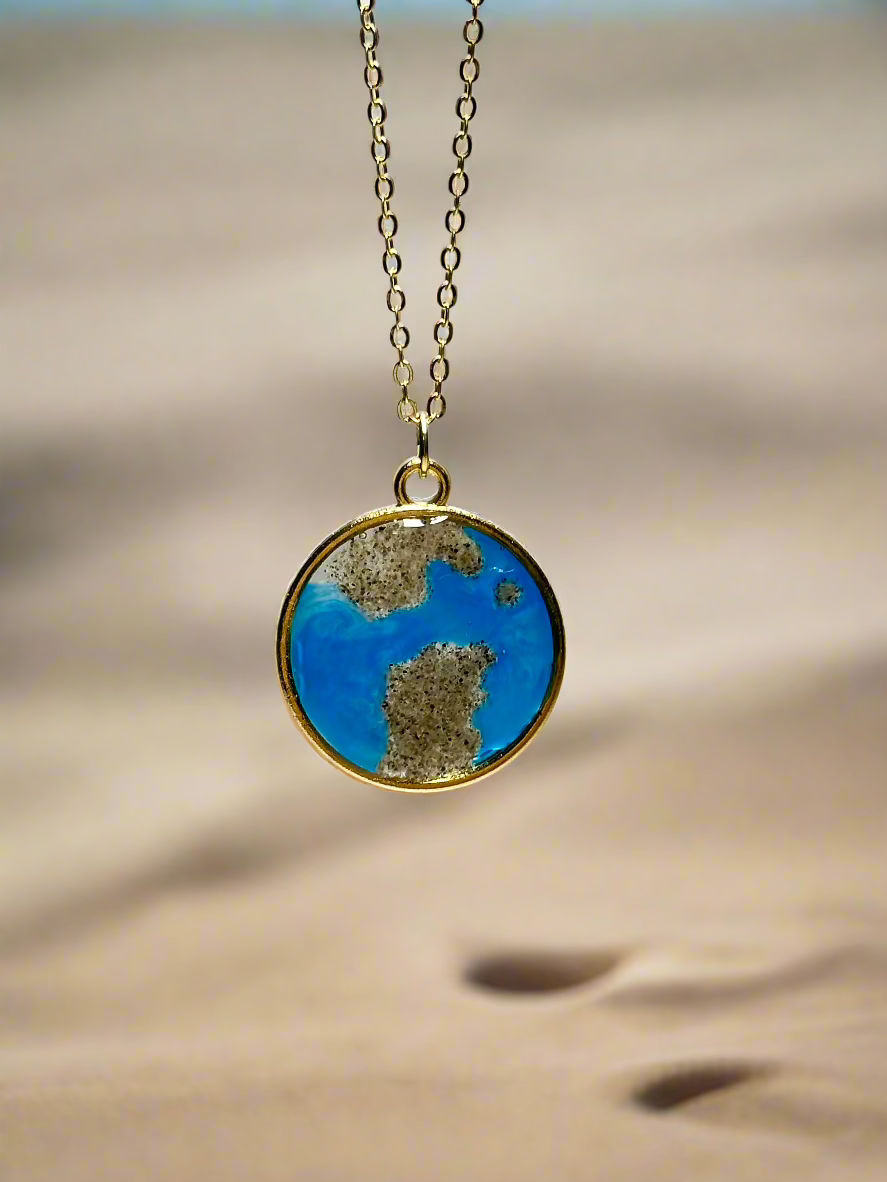 This is a round pendant necklace in gold with real california sand representing the coast of San Franciso.