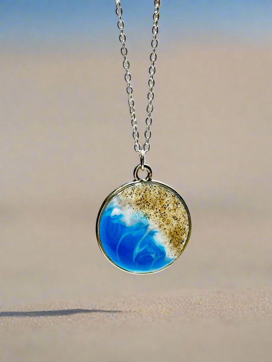 This is a photo of a necklace. Round silver pendant made with real SoCal sand and resin representing the coast of Ventura, CA.