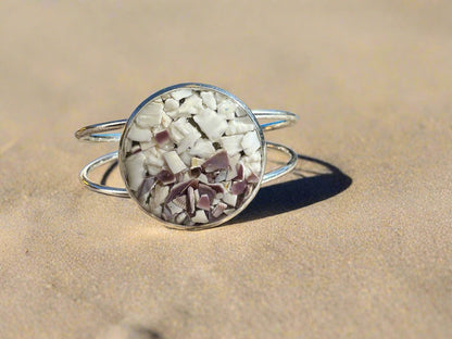 This is a picture of a silver cuff bracelet with white and purple seashells in the center bezel.